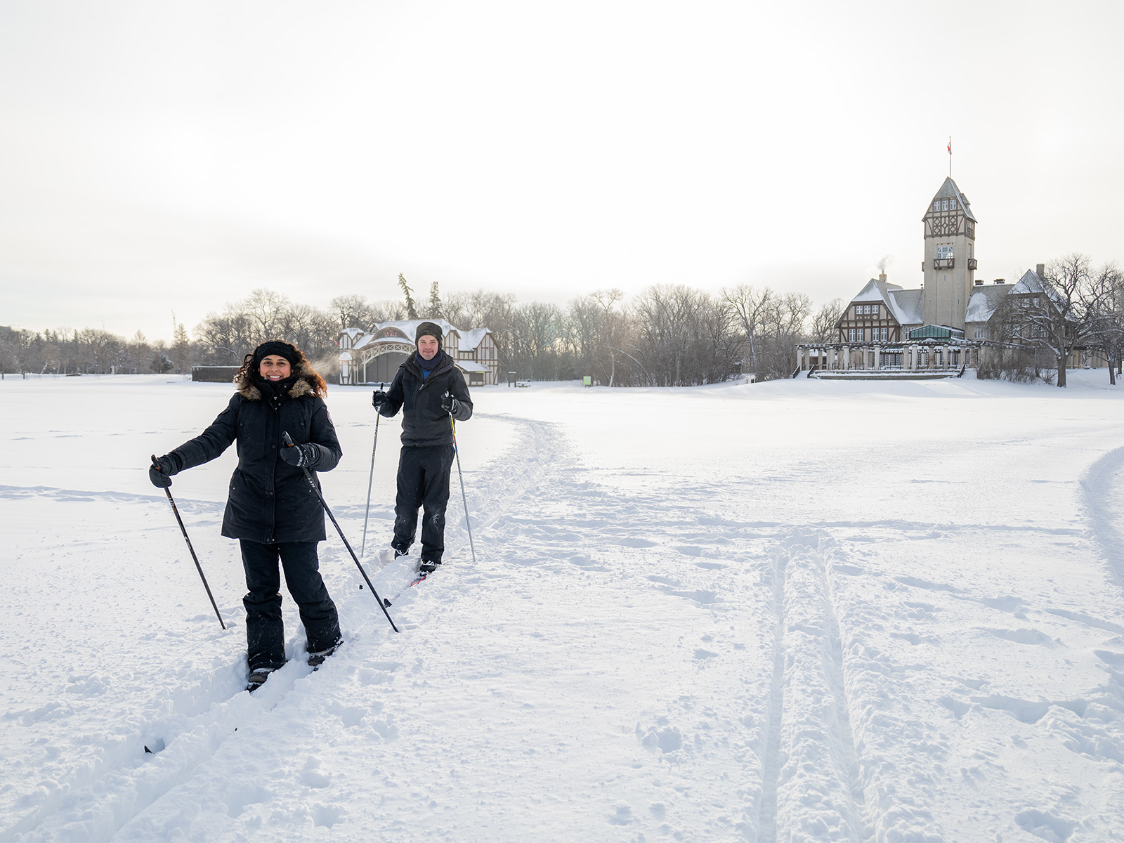 two people cross country ski in a field in front of the Lyric Theatre